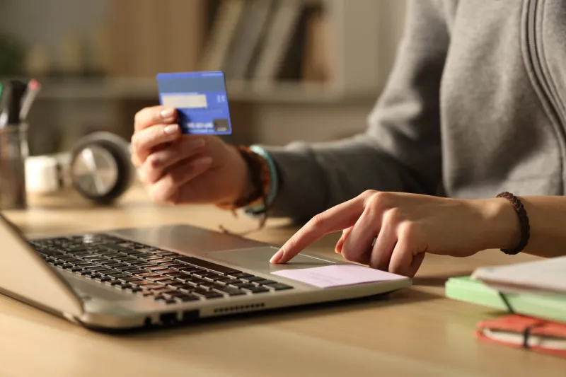 close up of student girl hands paying online with credit card on laptop at night sitting on a desk at home