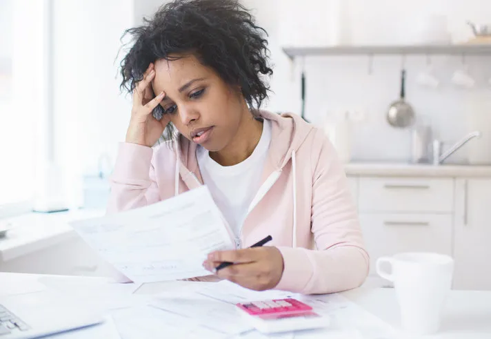 upset african american woman sitting at kitchen table with laptop, dealing with financial stress and pressure because of mortgage debt, worrying or feeling anxious no money concept