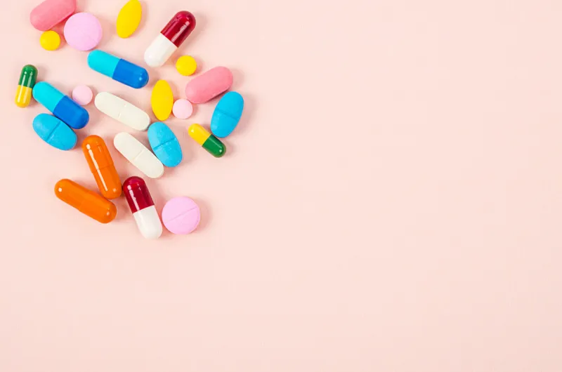 colorful tablets and capsules pills medicine heap on pink background