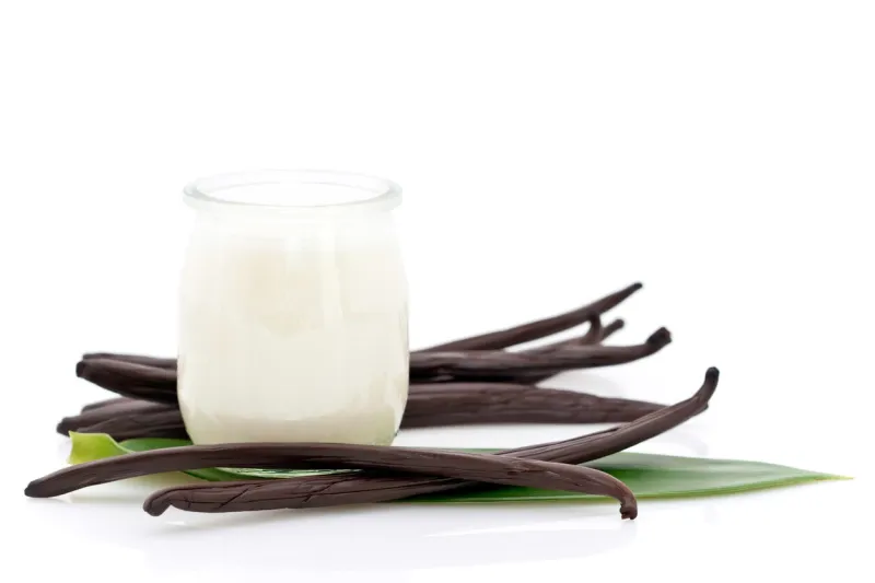 glass container of yogurt with fresh vanilla beans and leaf on white background