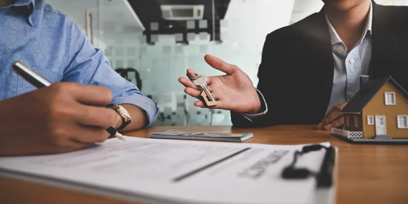 cropped image of real estate agent offer house insurance or house ownership to smart man in blue shirtn at the modern wooden table signing on agreement, broker seller dealer concept