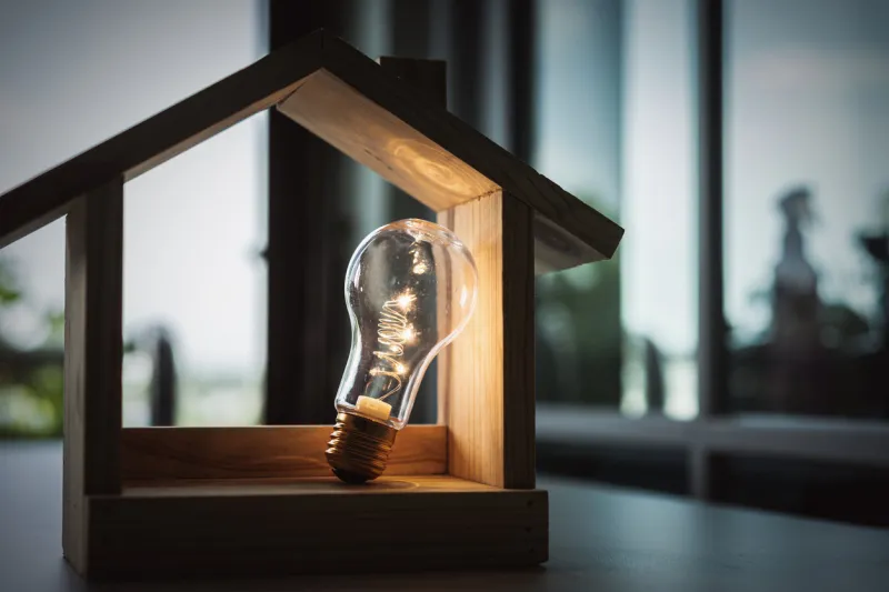 light bulb with wood house on the table, a symbol for construction, creative light bulb idea, power energy or business idea concept ecology, loan, mortgage, property or home