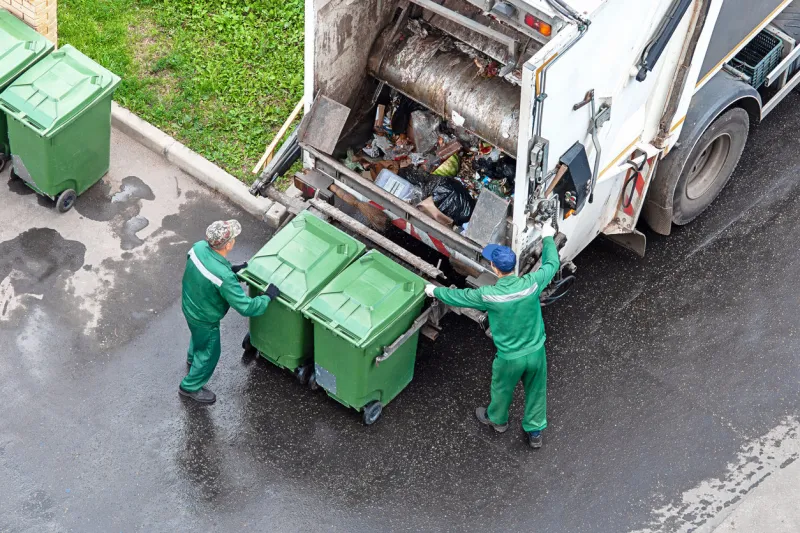 two workers loading mixed domestic waste in waste collection truck - moscow