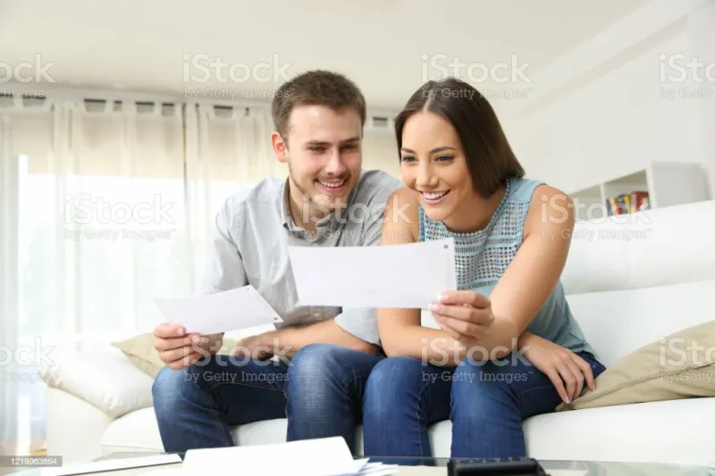 happy young couple looking and checking bills on a couch at home