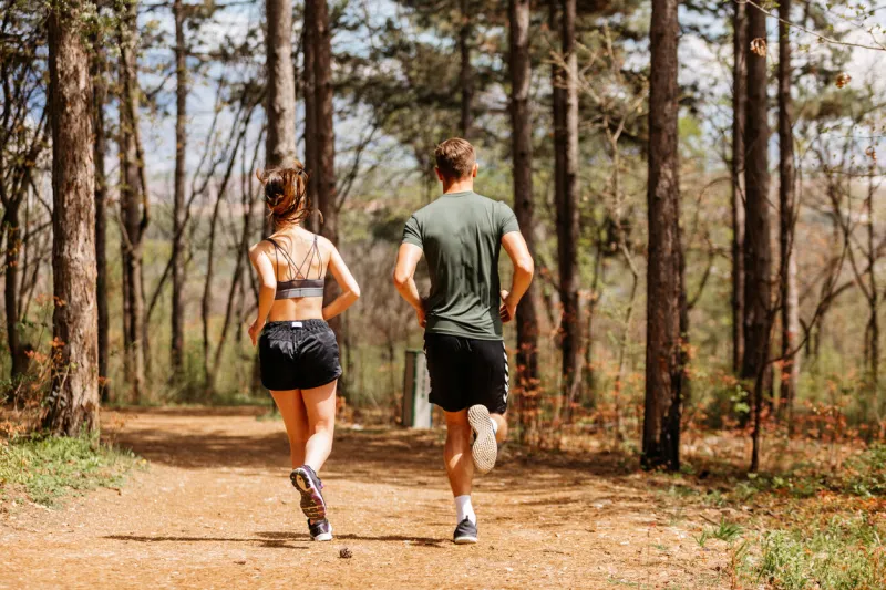 man and woman exercising and jogging together at the park happy and smiling as they run along the path during sunset on a warm summer day