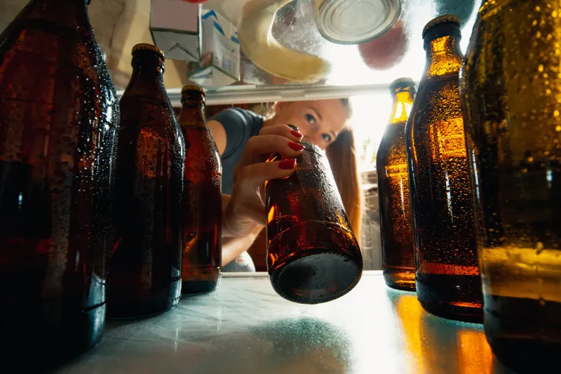 caucasian woman takes cold refreshing beer from out the fridge, inside view from fridge of hand holding the bottle alcohole, domestic life, entertainment, drink concept cold cola or beer bottles