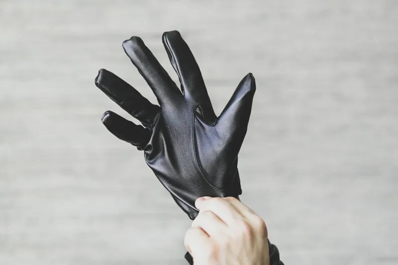 a man puts black leather gloves on his hands on a gray background leatherette gloves