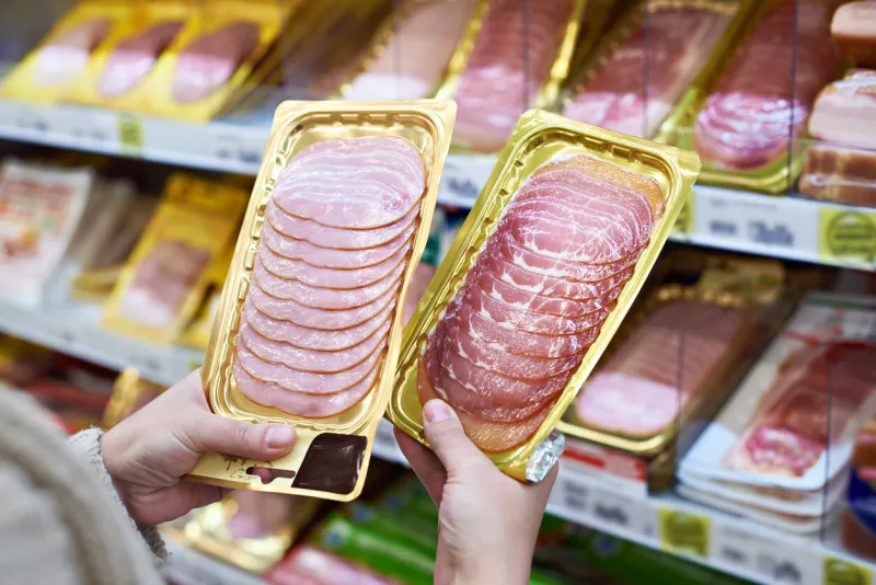woman chooses a slice of ham and meat in vacuum package at the grocery store