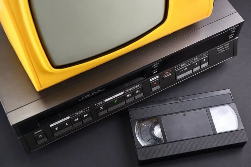 old yellow vintage tv with vcr and videotape on black background from 1980s, 1990s, 2000s stack
