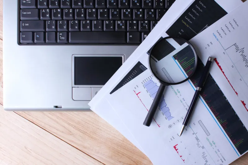 work at home a computer with a magnifying glass on a wooden table and analyzing the stock market