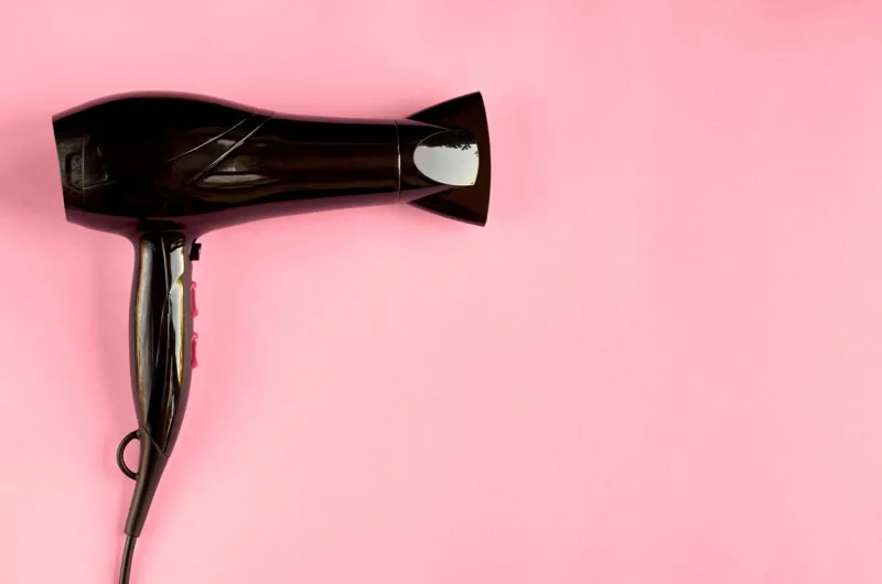 black hair dryer on pink background composition flat lay and top view photo