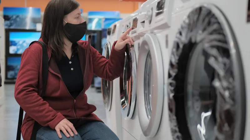 caucasian a woman in a black antivirus medical mask picks out washer at an electronics store the woman is wearing a red jacket and blue jeans