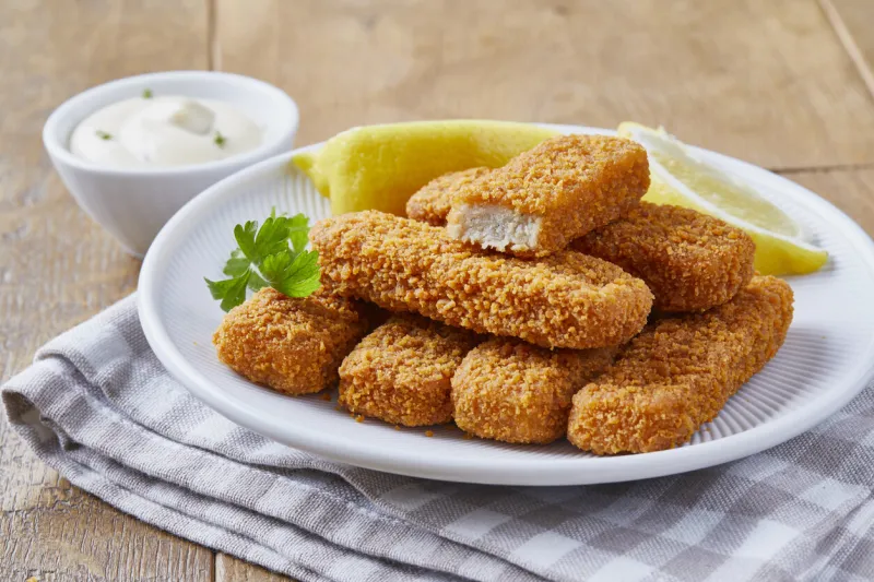 close up of a fish sticks with lemon slices, served on a dark brown wooden kitchen table
