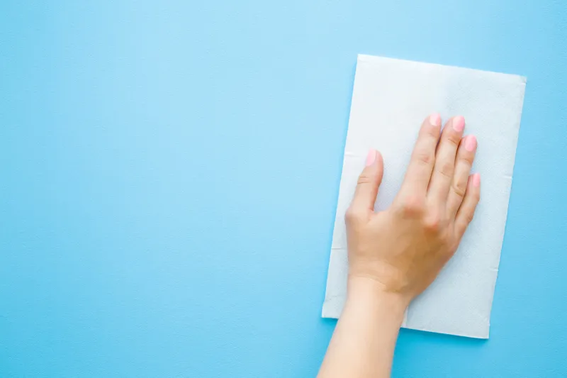 woman's hand wiping pastel blue desk with white paper napkin general or regular cleanup close up empty place for text or logo top view