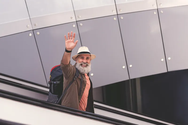portrait of outgoing unshaven old man flourishing arm while moving on travelling staircase