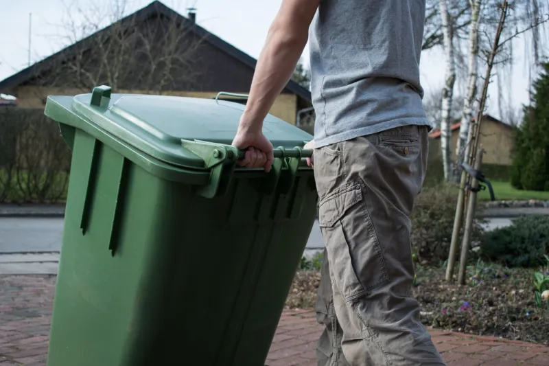 man pushing a green garbage bin