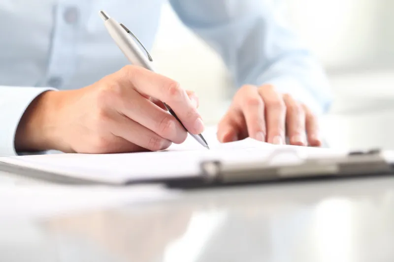 woman's hands writing on sheet in a clipboard with a pen, isolated on desk