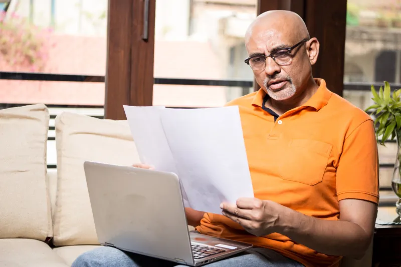 middle age man in casual wear working on laptop at home looking at the documents