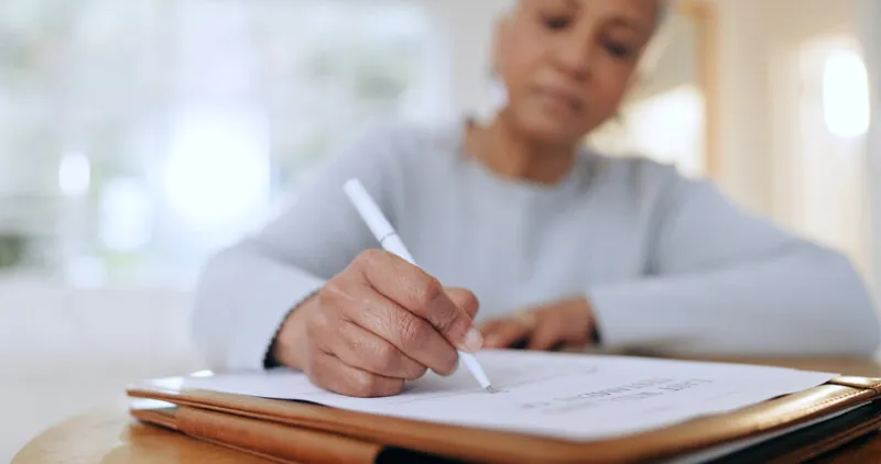 senior woman, sign and writing with documents, paperwork and application for life insurance policy person, hand and checklist for compliance, investment or will in retirement with signature in home
