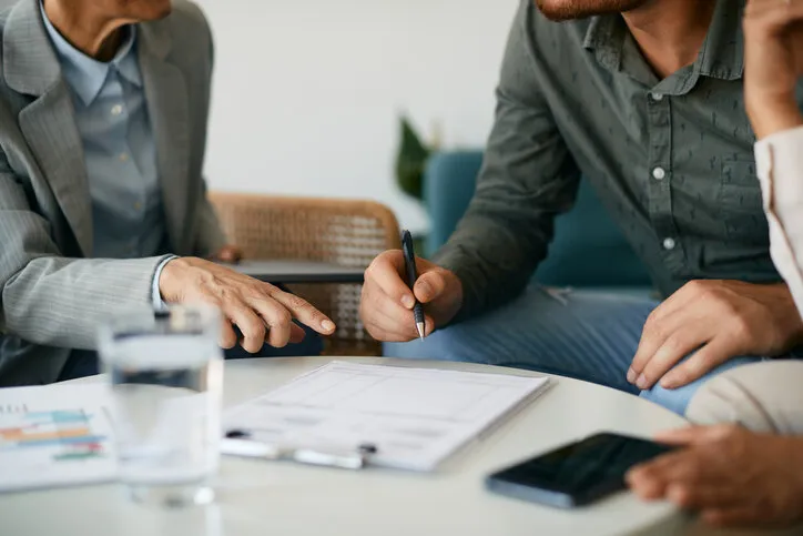 close-up of couple closing a deal with their financial advisor and signing paperwork during the meeting
