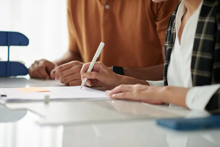 hands of spouses signing documents at meeting with social worker