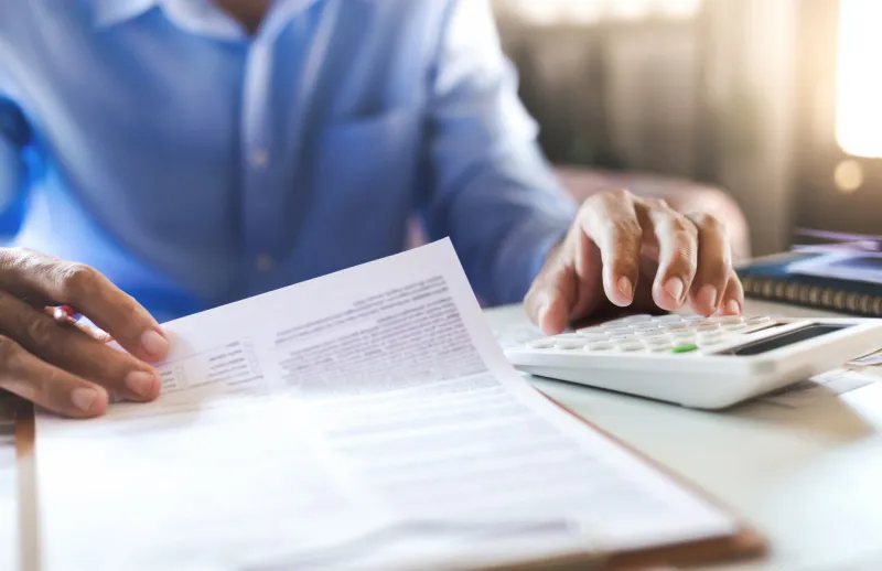 asian businessman on desk in office using calculator to calculate life insurance benefits or expenses from statement and financial report, accountant working in the office, close-up view
