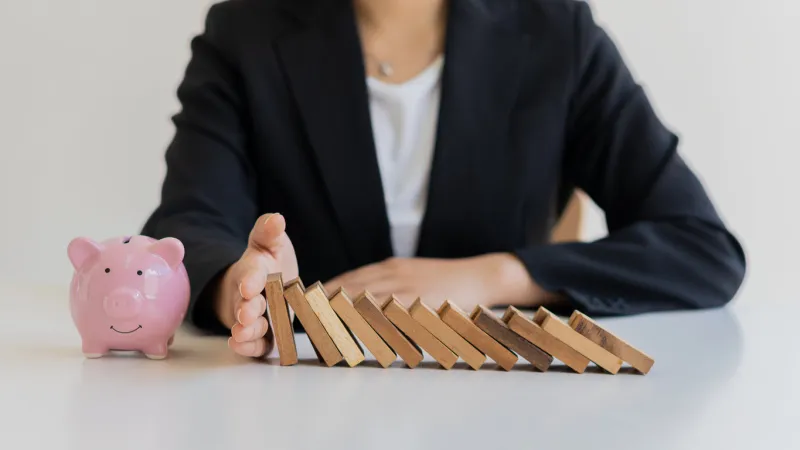 businesswoman protecting piggy bank from falling wooden blocks on the table, financial business concept