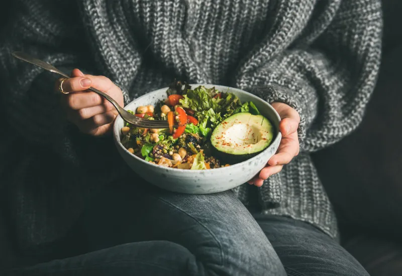 healthy vegetarian dinner woman in grey jeans and sweater eating fresh salad, avocado half, grains, beans, roasted vegetables from buddha bowl superfood, clean eating, dieting food concept