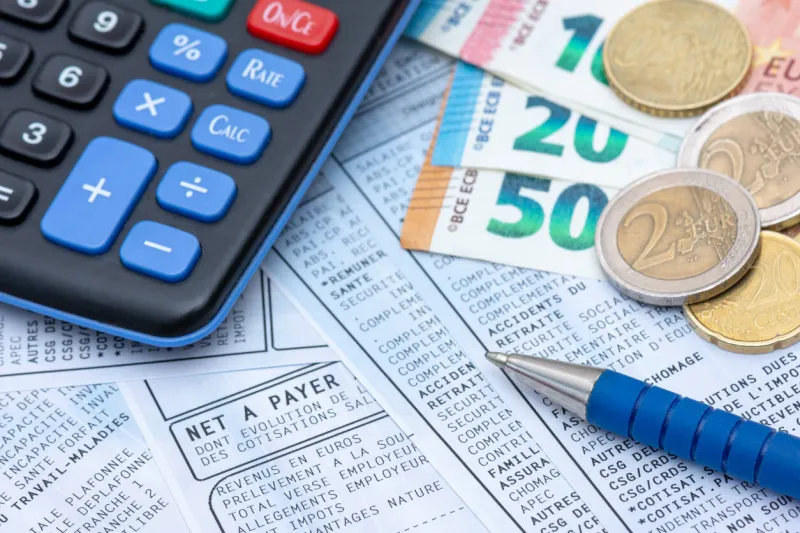 french payroll with social contributions and income tax deduction, mandatory in france since january 2019, along with a calculator, a pen, and euro coins and bank notes