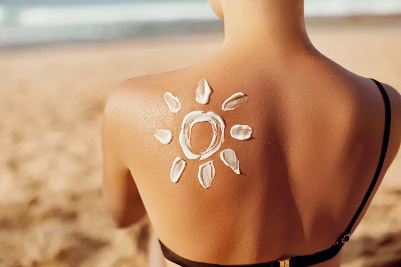 skin care sun protection woman apply sun cream woman with suntan lotion on beach in form of the sun portrait of female with drawn sun on a shoulder suncream girl holding moisturizing sunblock