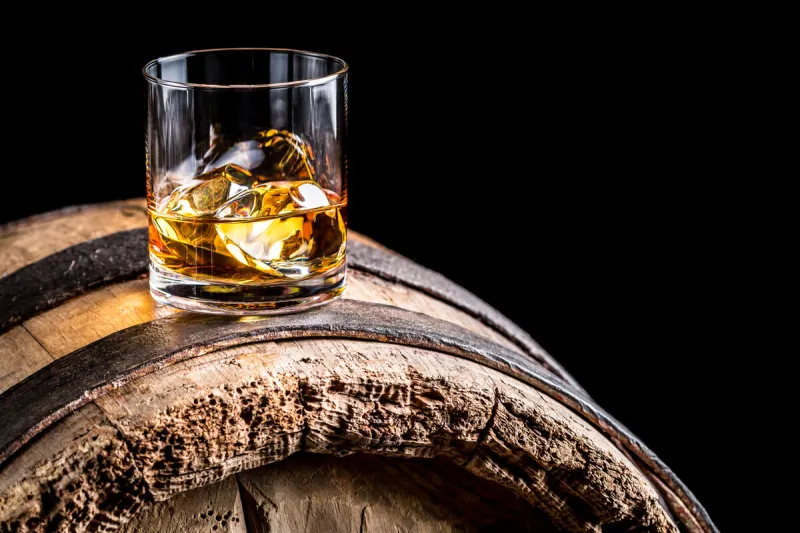 glass of whisky with ice on old wooden barrel