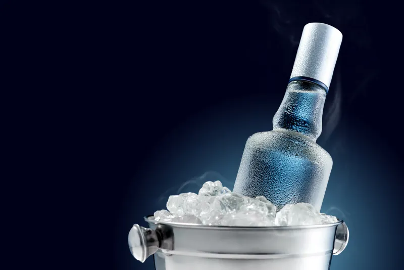 bottle of cold vodka in bucket of ice on dark background
