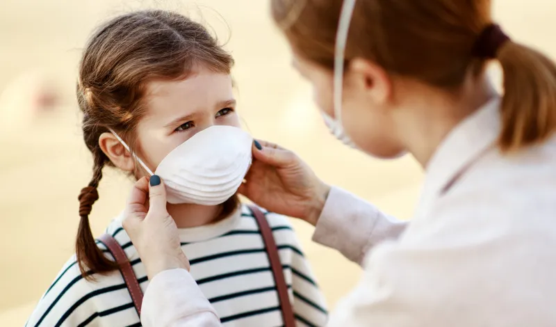 from above adult woman putting on medical mask of little girl while standing on city street during coronavirus pandemic