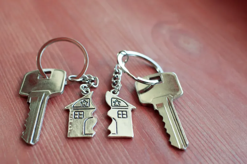 two keys with splitted or broken key rings with pendant in shape of house divided in two parts on wooden background with copy space dividing house when divorce, division of property, real estate heritage