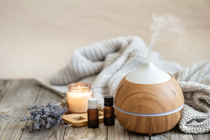 modern aroma oil diffuser on wood surface with knitted element, candle and lavender oil on a blurred background