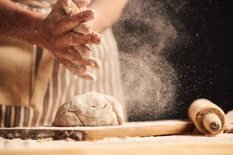 female baker hands making dough for bread with an apron roller