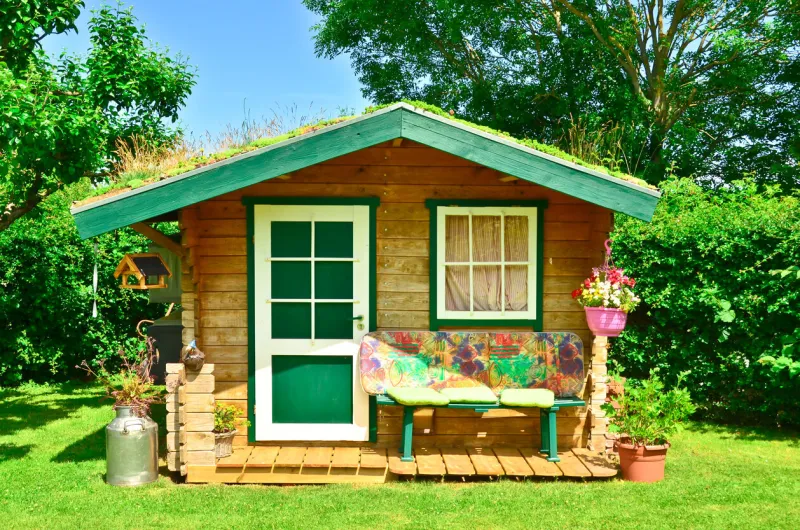 a light green and wooden small shed, gardenhouse, with a bench some tools around it