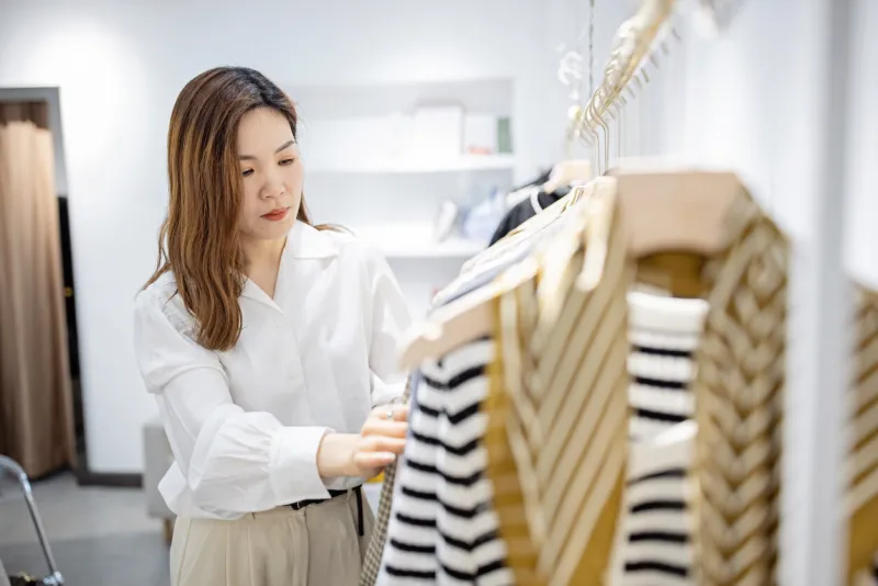 portrait of happy female asian entrepreneur working in her modern store with womenswear clothes, young chinese woman owner or consultant holding fashionable clothing while standing in brandy shop high quality photo
