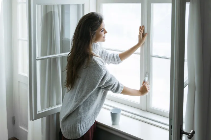 woman is opening window to look at beautiful snowy landscape outside