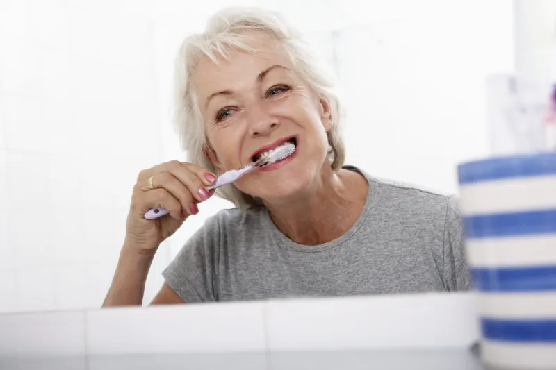 senior woman in bathroom brushing teeth at home