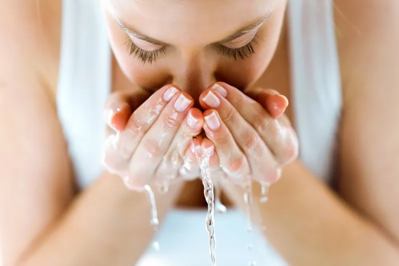 portrait of beautiful young woman washing her face splashing water in a home bathroom