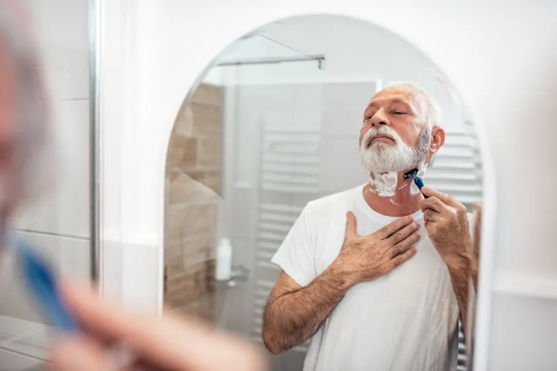 senior man shaving in the bathroom, reflection in the mirror image