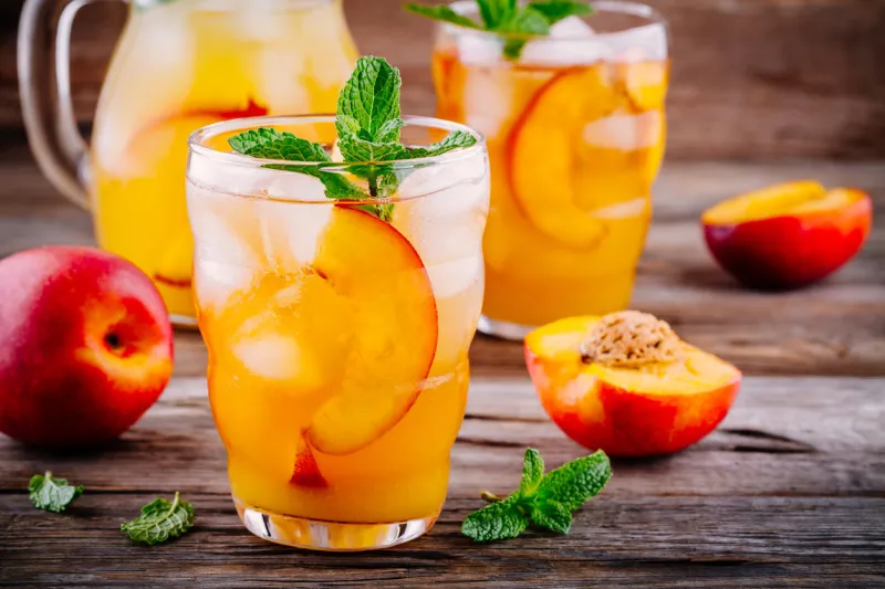 summer cold drinks  homemade peach ice tea with ice cubes, and mint in glass on wooden background