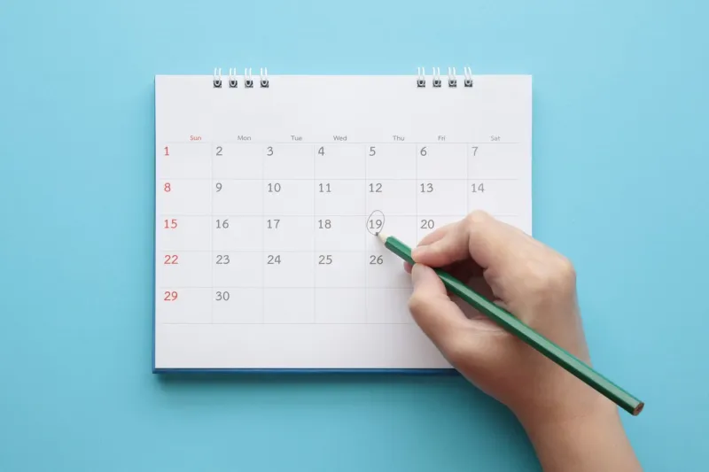 hand with pencil mark on calendar date on blue background