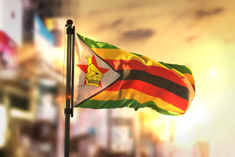 zimbabwe flag against city blurred background at sunrise backlight
