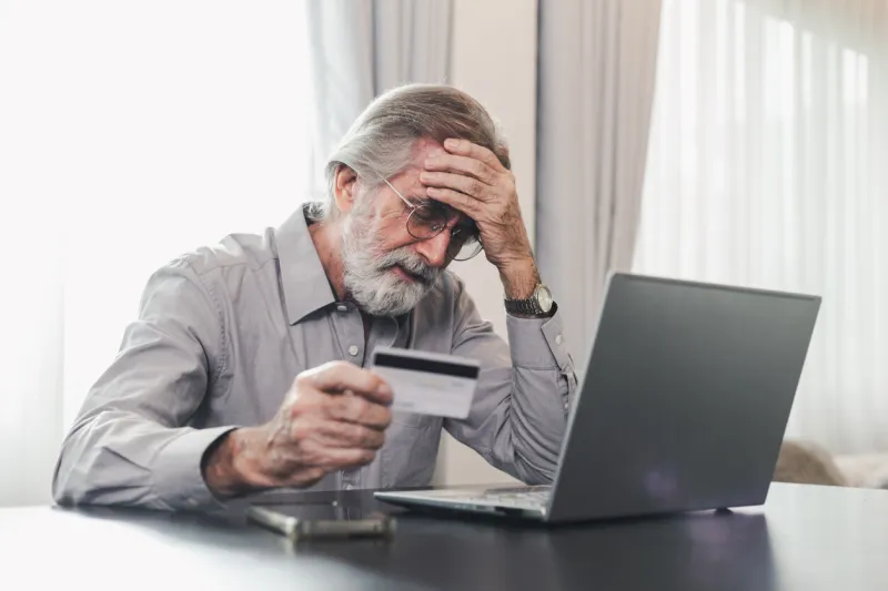 upset senior elderly man holding credit card by laptop having trouble worry finance safety data or online payment security bank client concerned about problem with credit card, financial fraud threat