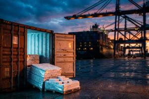 A dramatic, high-contrast cinematic shot of a massive cargo port at twilight. In the foreground, a p