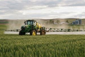 image agricole d'un tracteur qui fait un épandage de pesticides dans un champ