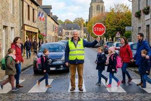 un retraité vêtu d'un gillet jaune et qui fait traverser des enfants à un passage piéton à la sortie