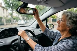 Une femme de 70 ans au volant d'une voiture à l'arrêt. Elle règle son rétro viseur
